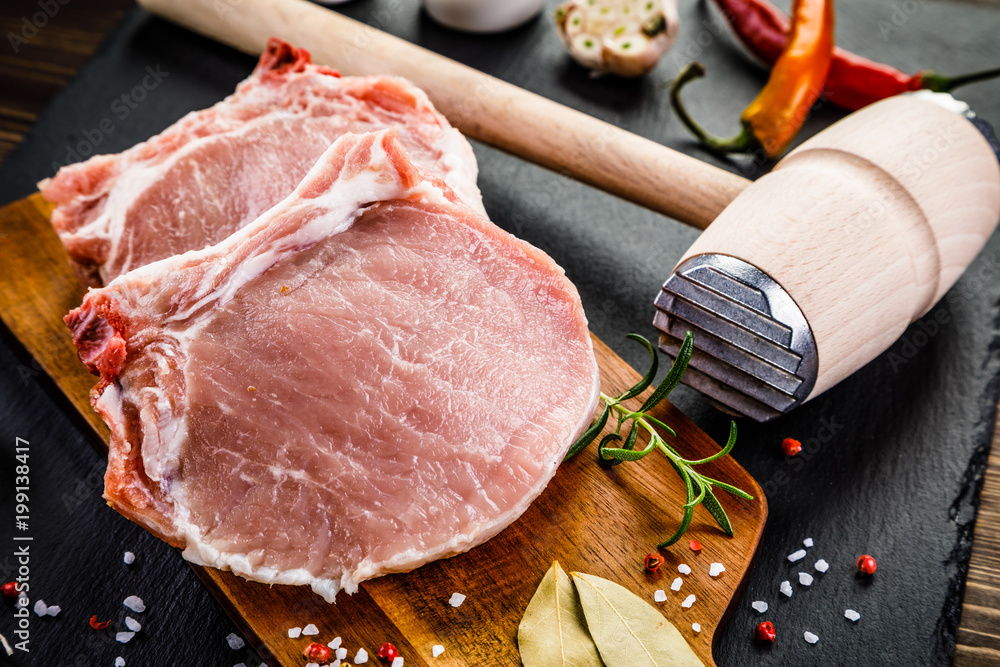 Fresh raw pork chops on black stone on wooden background Fresh raw pork chops on black stone on wooden background