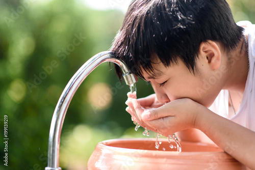 Asian boy take water from faucet to wash his mouth.