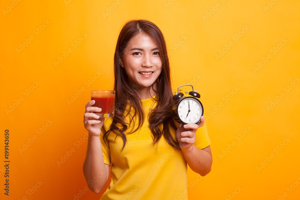 Young Asian woman with tomato juice and clock in yellow dress Young Asian woman with tomato juice and clock in yellow dress