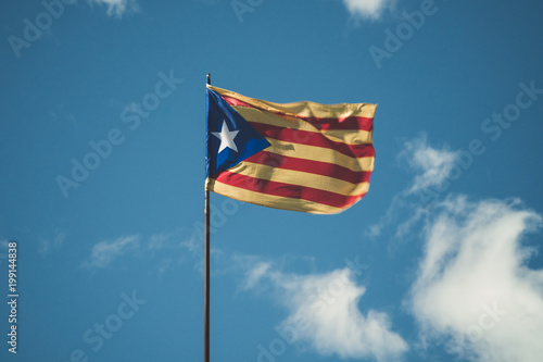 An independentist flag of Catalonia is waving on a pole. The sky is blue with some clouds. photo