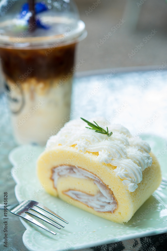 Coconut roll cake, gelly and coconut meat inside. coconut roll cake on dish with coffee in background Coconut roll cake, gelly and coconut meat inside. coconut roll cake on dish with coffee in background