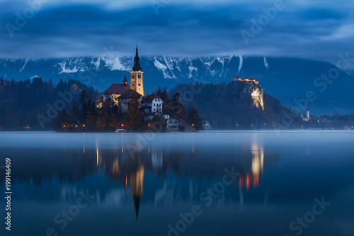 Fototapeta Naklejka Na Ścianę i Meble -  Bled lake and castle with water reflection at dawn with moody cloudy sky, Slovenia, Europe