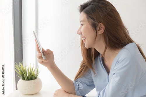 Asian women are smiling using smartphone at home.