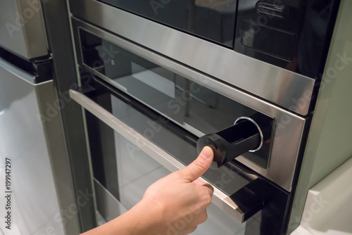 Hand pressing button on silver black wall oven with built-in microwave.