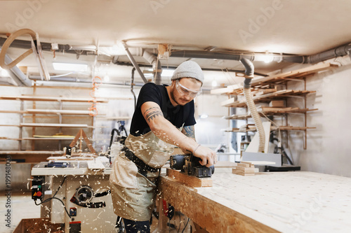 Fotografie Carpenter working with electric planer on wooden plank in workshop
