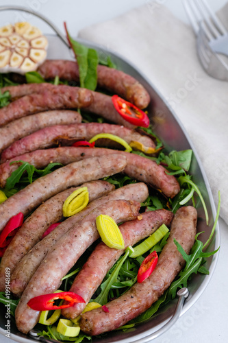 Grilled sausages with vegetables, fresh herbs and spices on white background.