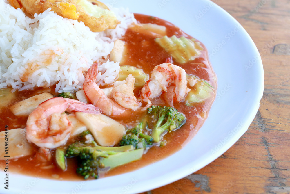 stir fried shrimp and Broccoli in thai red curry paste sauce with rice, Curry fried shrimps and cooked rice in white dish closeup on wooden table. Thai style food. stir fried shrimp and Broccoli in thai red curry paste sauce with rice, Curry fried shrimps and cooked rice in white dish closeup on wooden table. Thai style food.