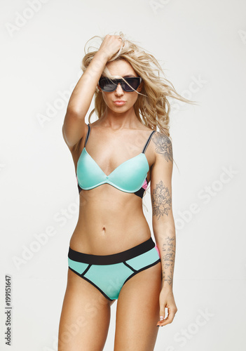 beautiful woman with long blond hair, has confident expression, wears turquoise swimsuit, sunglasses, isolated over white background. © Ilshat