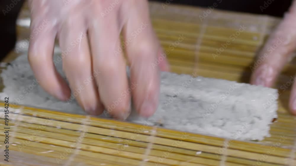 Close up of gloved hands of unrecognizable cook wrapping sushi with bamboo mat Close up of gloved hands of unrecognizable cook wrapping sushi with bamboo mat