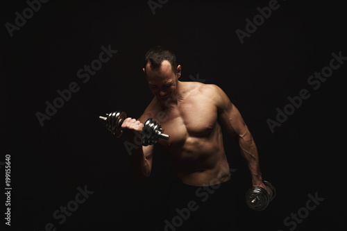 Strong athletic man with dumbbell showes naked muscular body