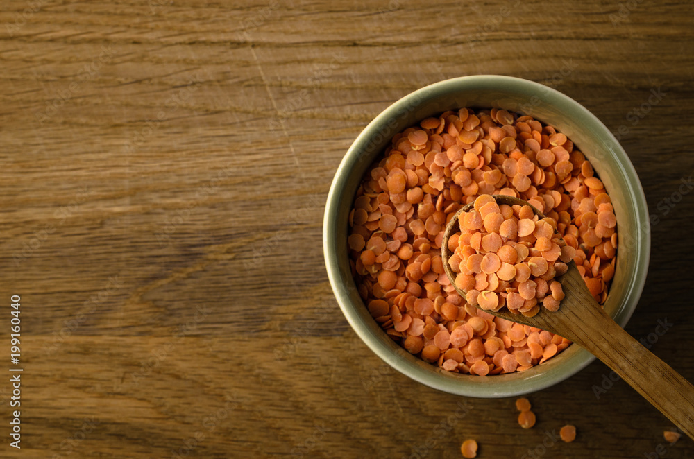 Overhead of Spoon Raising Red Lentils from Green Bowl on Oak Wood Background Overhead of Spoon Raising Red Lentils from Green Bowl on Oak Wood Background