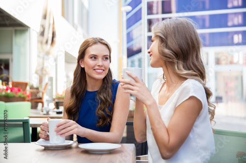 communication and friendship concept - smiling young women drinking coffee at street cafe