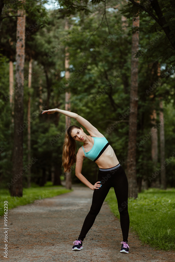 fitness training outdoors in the Park. A young girl in sporty leggings and t-shirt makes a warm-up before Jogging fitness training outdoors in the Park. A young girl in sporty leggings and t-shirt makes a warm-up before Jogging