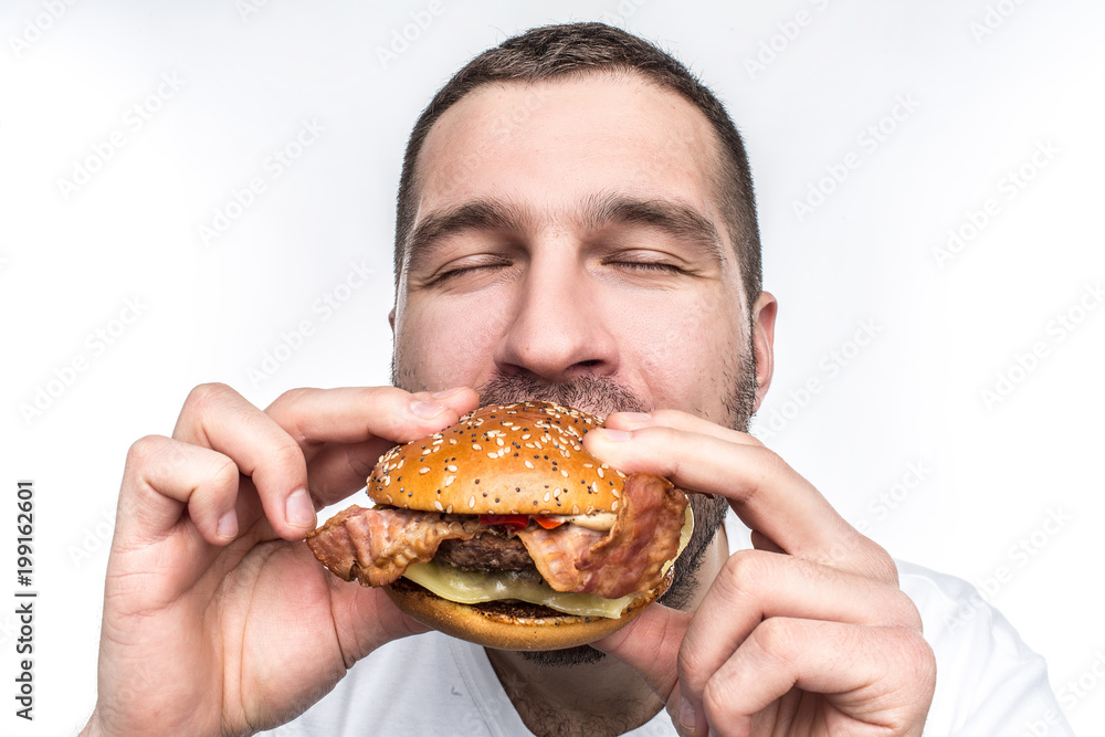 Weird and bizarre man is eating fat and juicy hamburger. It is not a healthy food but the guy likes it very much. His face is very emotional. Isolated on white background. Weird and bizarre man is eating fat and juicy hamburger. It is not a healthy food but the guy likes it very much. His face is very emotional. Isolated on white background.