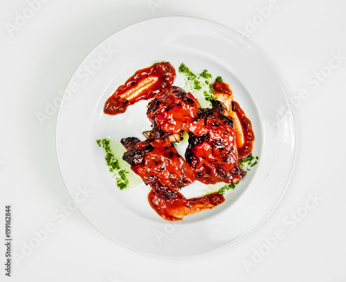 plate with fried ribs under tomato sauce with greens.