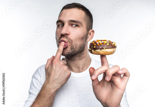 A picture of young guy that want to calm his hunger He decided to eat tasty but oily chocolate donut that he has on his finger. He can t wait to eat it. Isolated on white background.