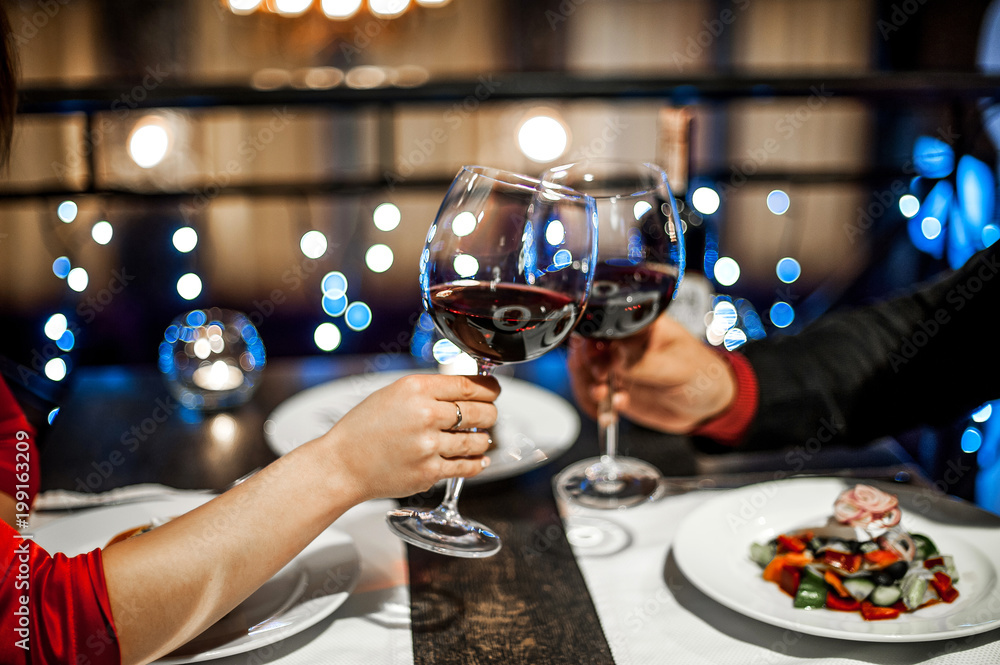 Hands with glasses of wine on a date at a table in a restaurant