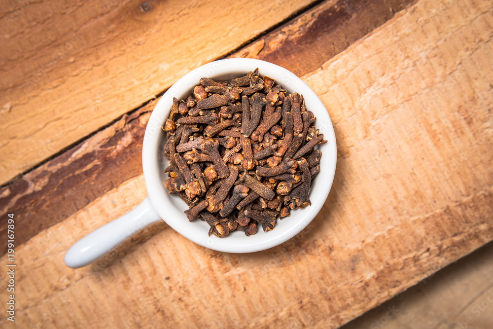 Exotic spices concept organic cloves in white cup on wood background with copy space Exotic spices concept organic cloves in white cup on wood background with copy space