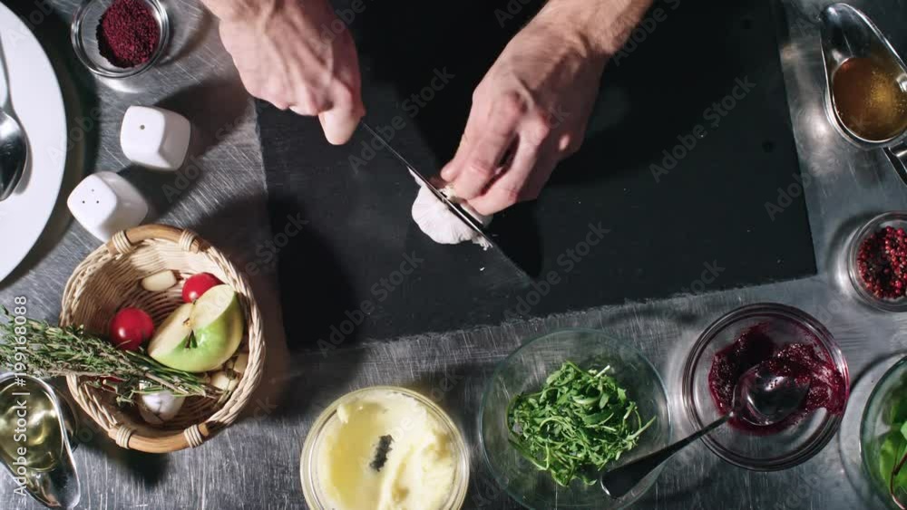 Top view of unrecognizable cook cutting garlic cloves on tabletop in kitchen Top view of unrecognizable cook cutting garlic cloves on tabletop in kitchen