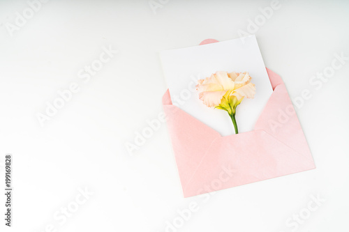 Minimal composition with a pink envelope, white blank card and eustoma flower on a white background. Mockup with envelope and blank card. Flat lay. Top view.