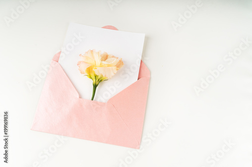 Minimal composition with a pink envelope, white blank card and eustoma flower on a white background. Mockup with envelope and blank card. Flat lay. Top view.