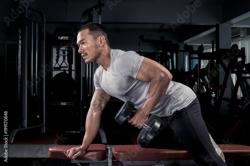 Muscular builder man training his body with dumbbell in Modern fitness center