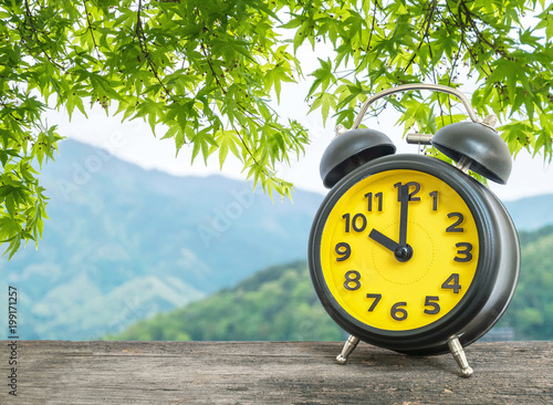 Closeup black and yellow alarm clock in ten o'clock on leaves and mountain view textured background