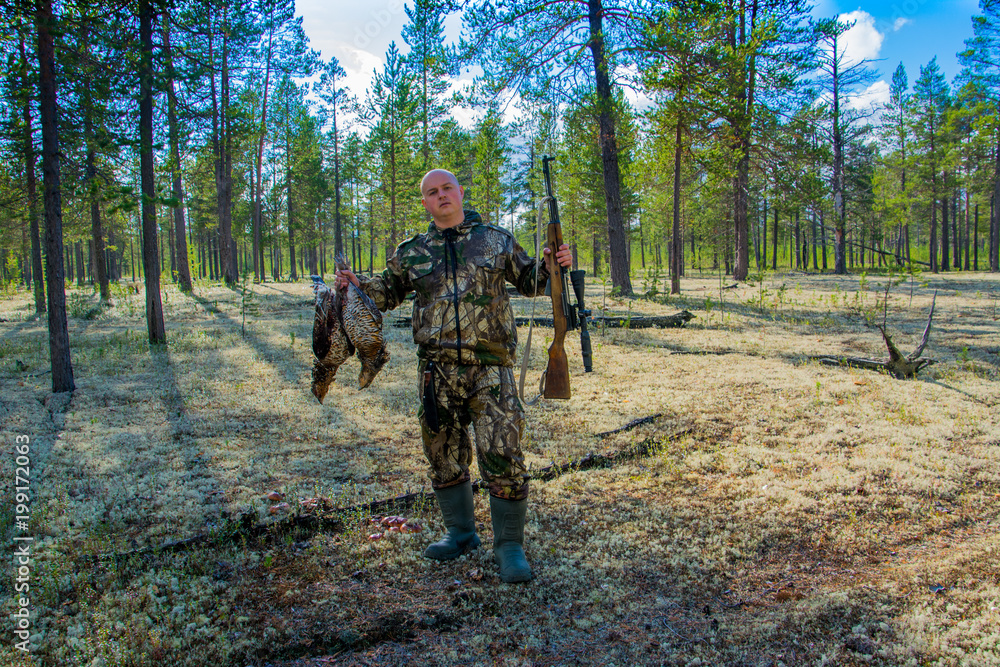 The hunter sitting wiht rifle and wildfowls. Hunting on the capercaillie. Yamal.