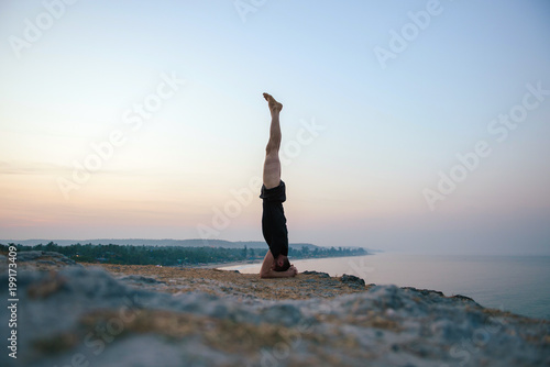 Healthy man practicing yoga under the beach at sunset.