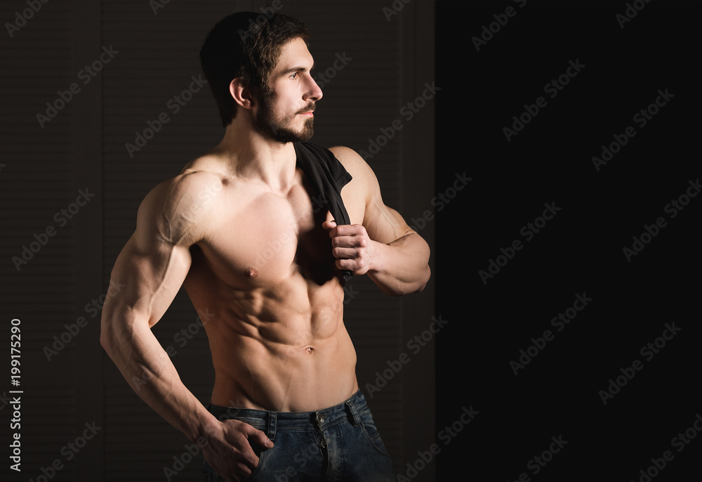 Portrait of shirtless muscular man in a jeans. Young male hunk showing his perfect body and muscles on black background.