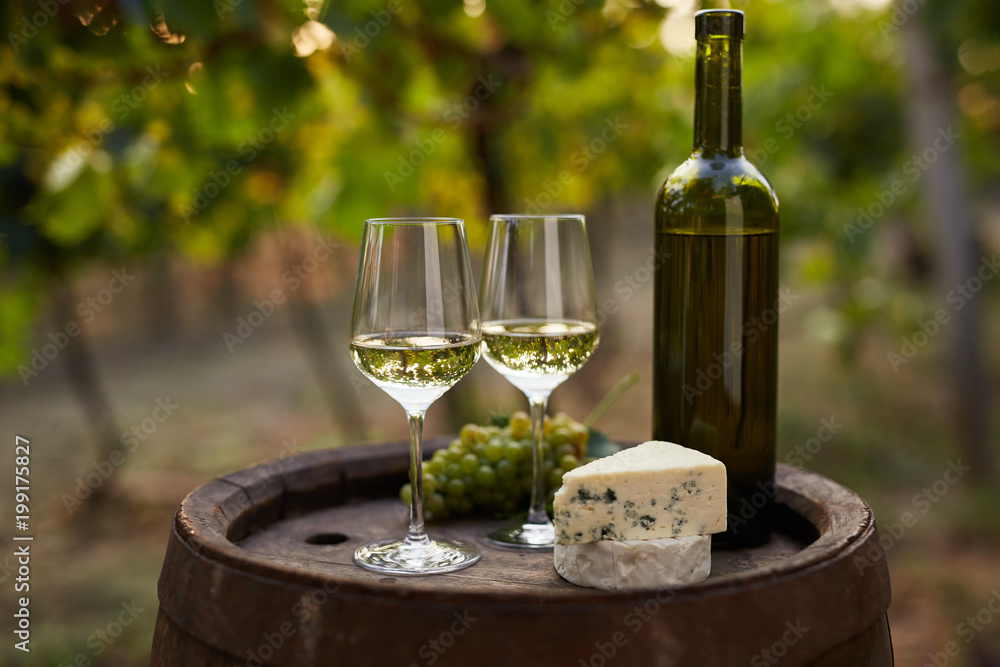 Pair of white wine glasses on wooden barrel with grapes