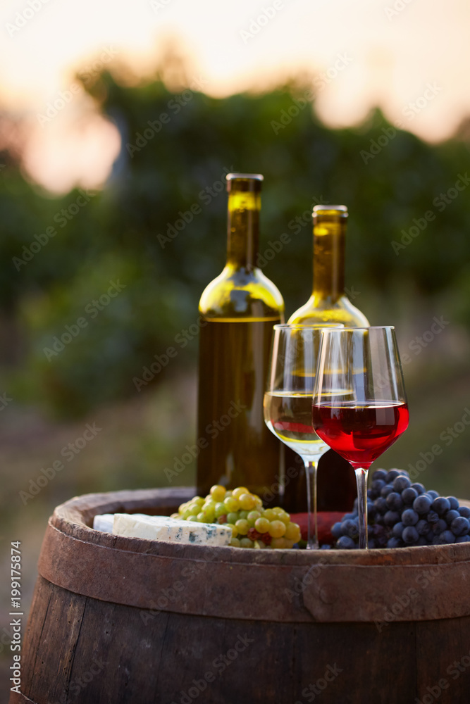 Pair of wine glasses and bottles on old barrel with bunch of grapes