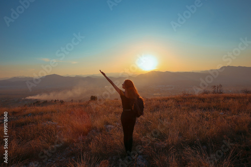 Sunset mountain. Tourist Free happy  woman outstretched arms with backpack enjoying life in wheat field. Hiker cheering elated and blissful with arms raised.