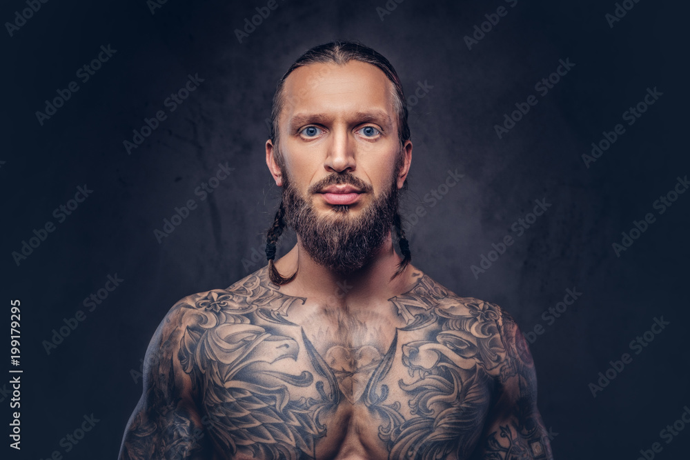 Fototapeta premium Close-up portrait of a muscular bearded tattoed male with a stylish haircut, isolated on a dark background.