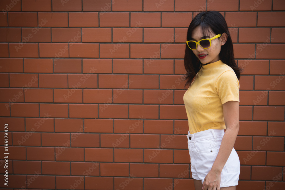 Portrait asian hipster girl on brick wall background,Thailand people wear yellow dress Portrait asian hipster girl on brick wall background,Thailand people wear yellow dress