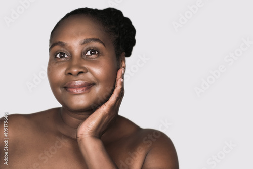 Smiling African woman touching her skin against a gray background