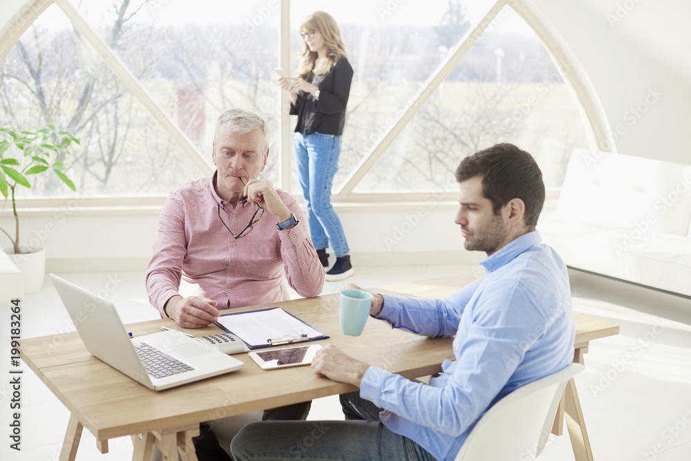 Close-up ofmiddle aged businesswoman consulting with senior manager and young assistant while sitting at office desk and working together on new project. Teamwork. Close-up ofmiddle aged businesswoman consulting with senior manager and young assistant while sitting at office desk and working together on new project. Teamwork.
