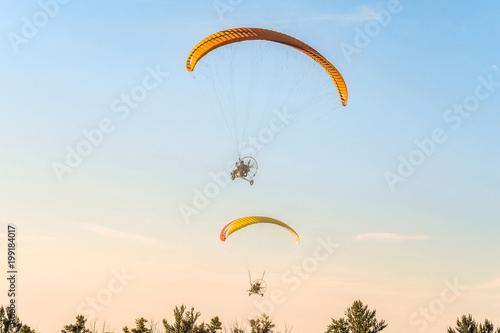 Flight of two motor paragliders trike skyward. Flight on motor gliders in the blue sky over the green trees.