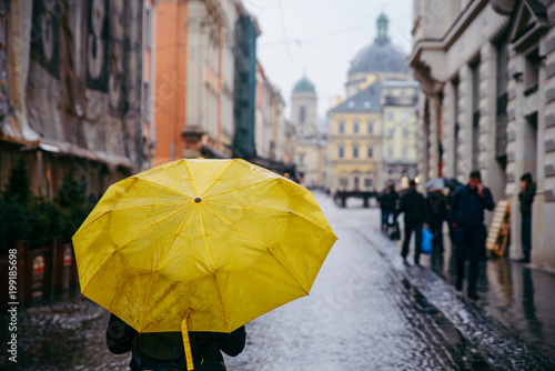 woman walk by old european streets in rainy weather with yellow umbrella. copy space © phpetrunina14
