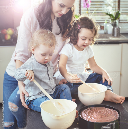 Cheerful mother teaching her children how to bake a cake