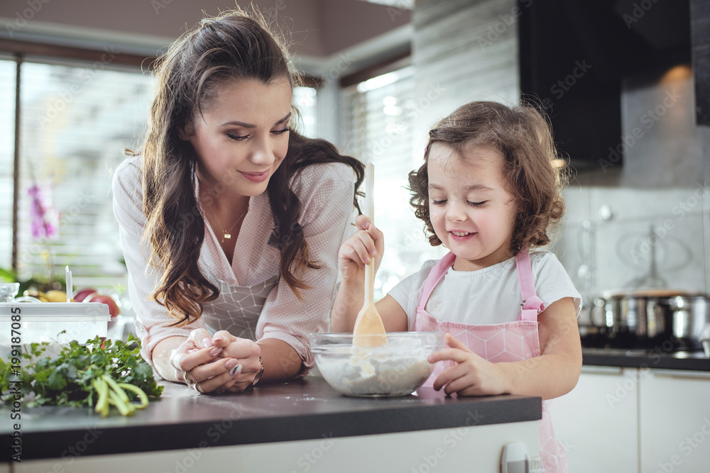 Mother watching her daughter whisking dough Mother watching her daughter whisking dough