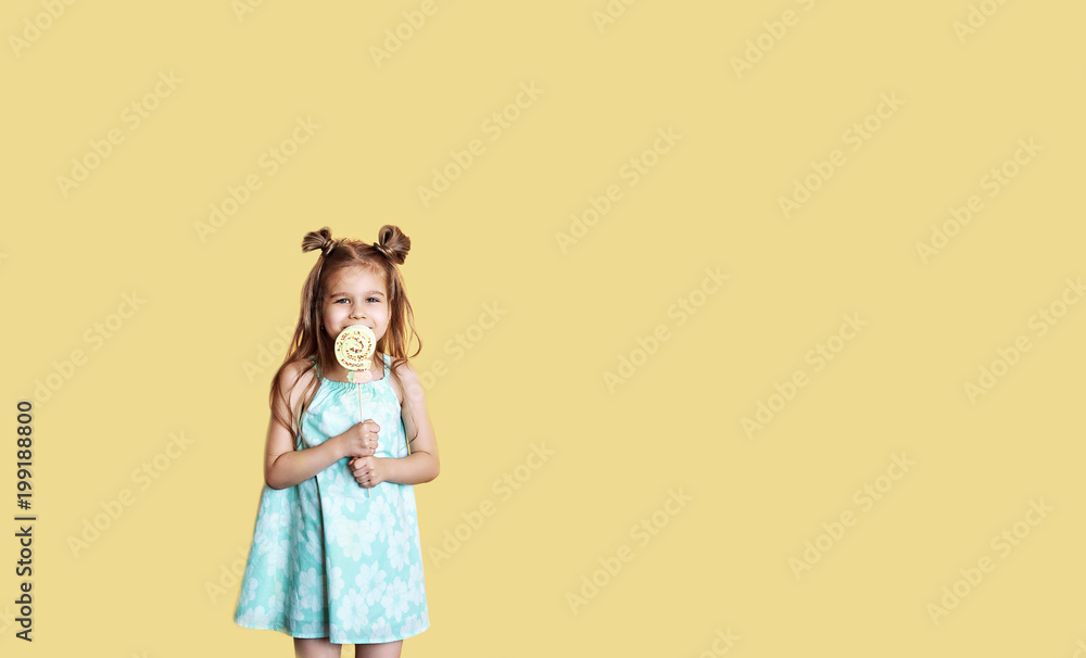 Portrait of a beautiful smiling little girl. Girl with big sweets on a yellow background with copy space Portrait of a beautiful smiling little girl. Girl with big sweets on a yellow background with copy space