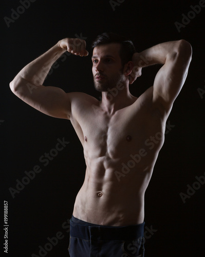 young strong man with muscles on black background