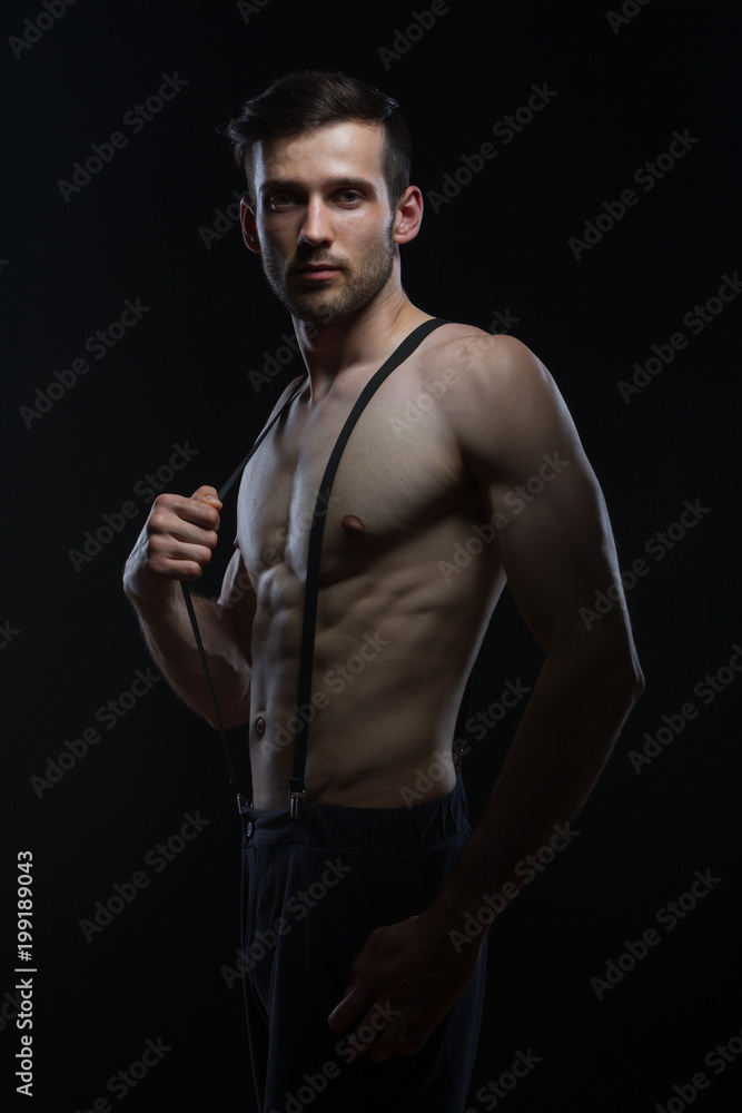 Naklejka premium young man with muscles with braces on pants on black background