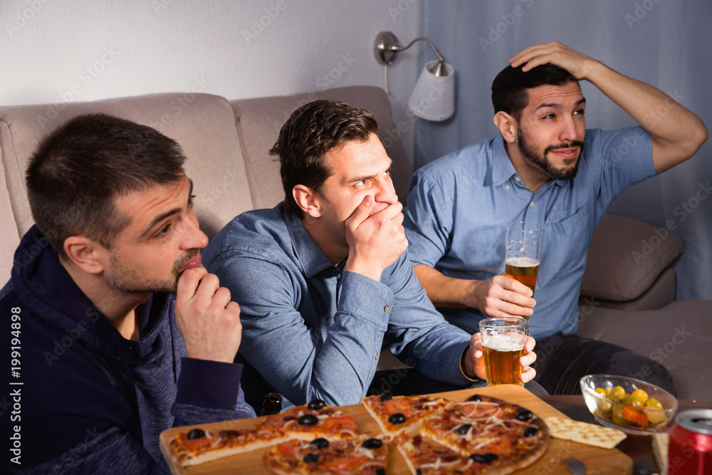 Worried concentrated men watching sporting match on tv with beer