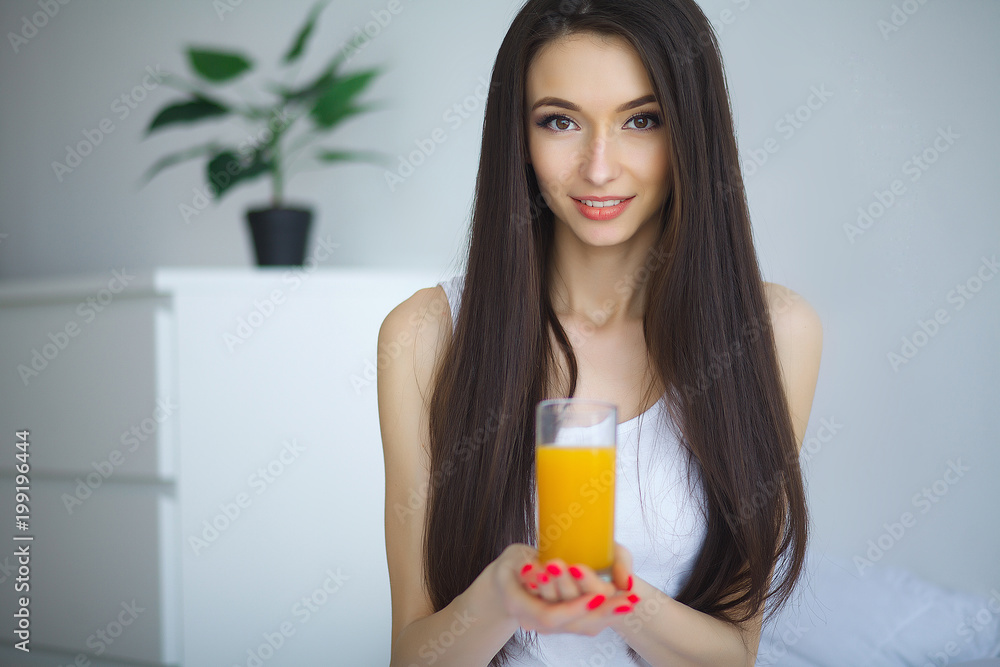 Cheerful woman drinking an orange juice sitting on her bed at home Cheerful woman drinking an orange juice sitting on her bed at home