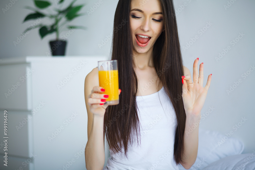 Cheerful woman drinking an orange juice sitting on her bed at home Cheerful woman drinking an orange juice sitting on her bed at home