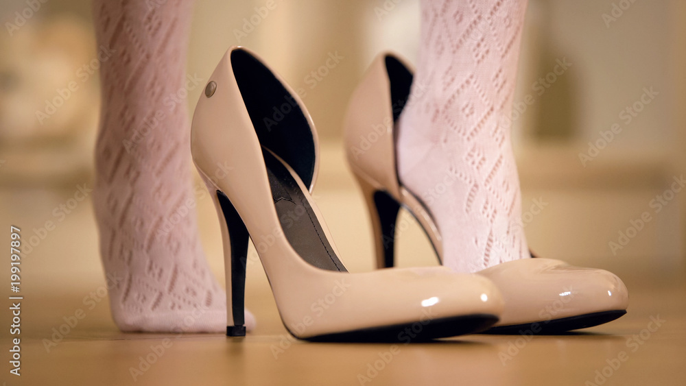 Feet of little girl putting mothers high heel shoes on and walking