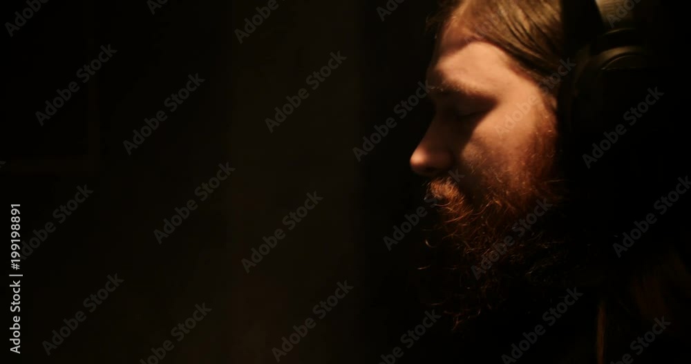 A bearded man in the darkness smokes an electronic cigarette and listens to music A bearded man in the darkness smokes an electronic cigarette and listens to music
