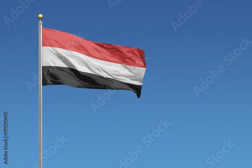 Fotografie Yemen flag waving in front of a clear blue sky